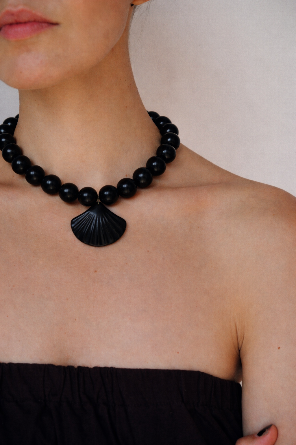Black beaded necklace with a shell pendant on a person wearing a black strapless top.